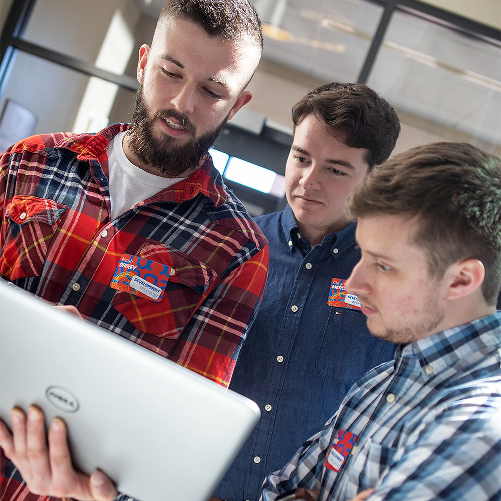 Three students stand around a laptop planning out their next steps.