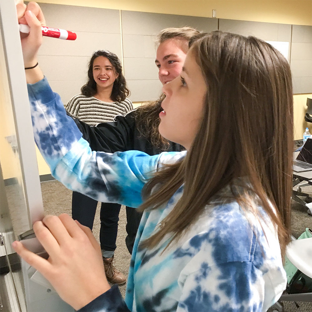 Three students gather at a whiteboard to strategize for a project.