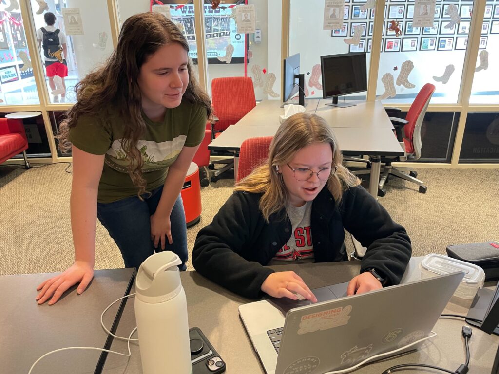 Two people are looking at a computer, one assisting the other.